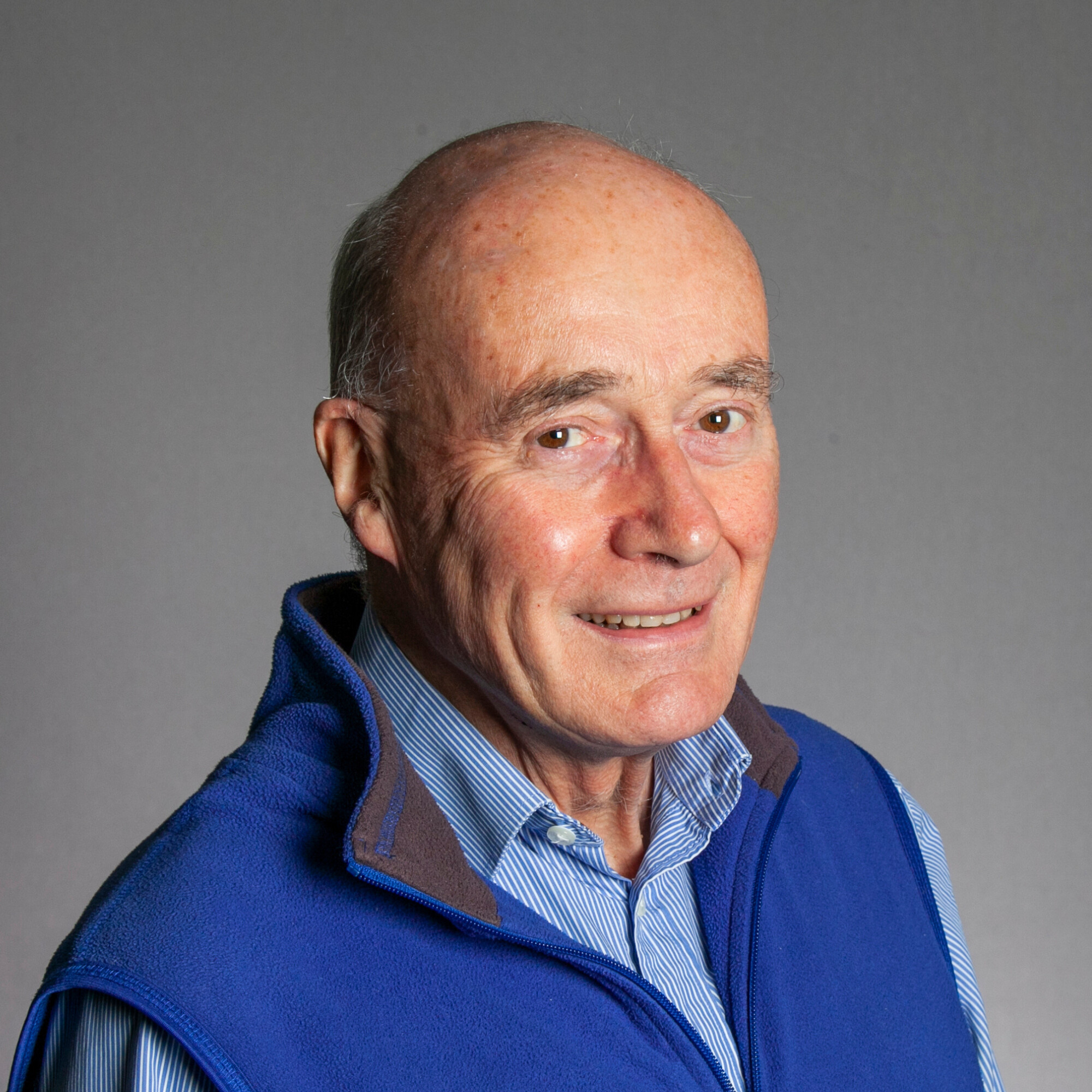 Photo of a white man smiling with a light blue shirt and a royal blue gillet on