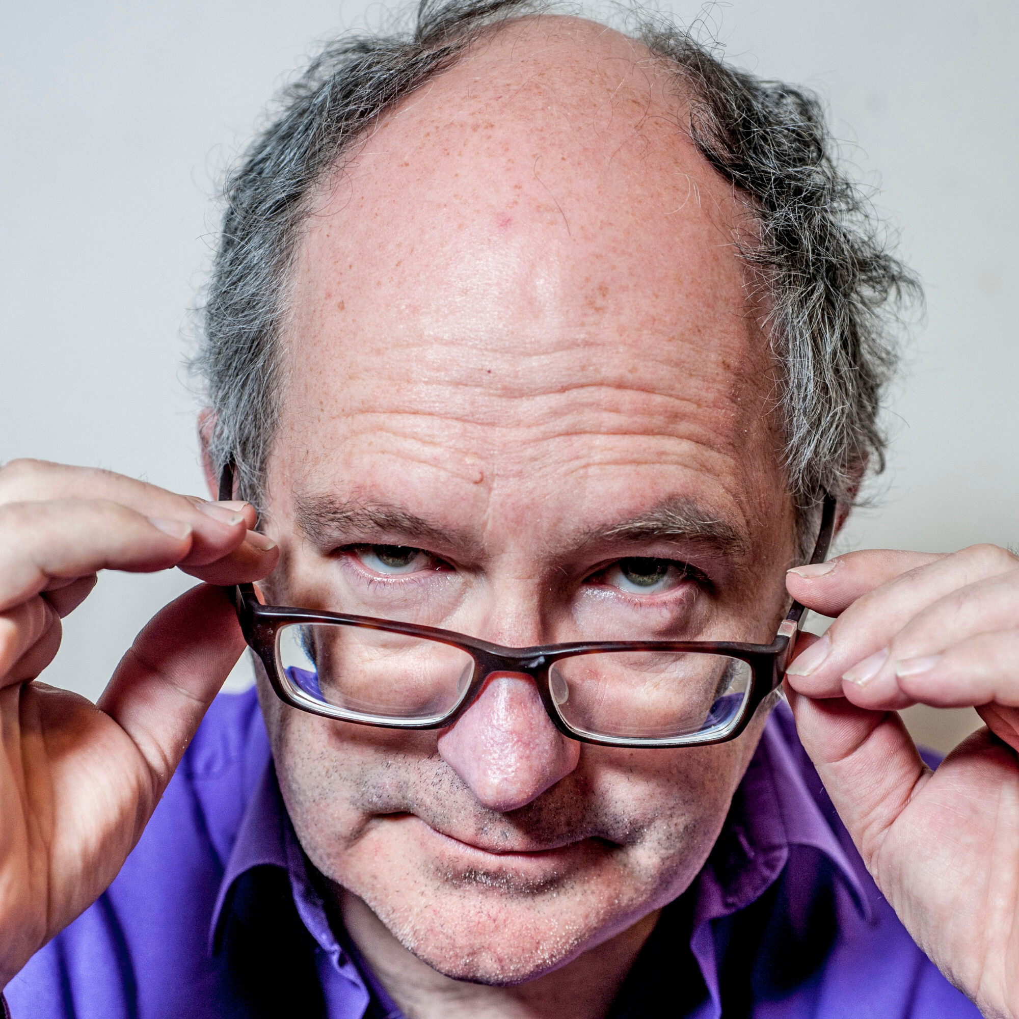 Headshot of John Lanchester lowering his glasses and peering over them
