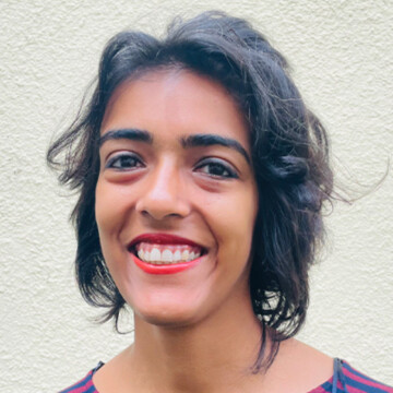 A woman with brown skin and shoulder-length dark brown hair is smiling widely. She is wearing red lipstick.