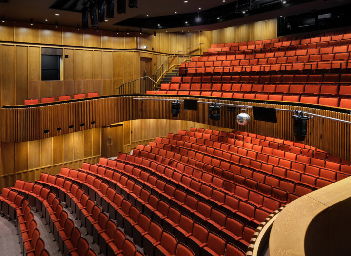 A theatre auditorium with red seats and low lighting.