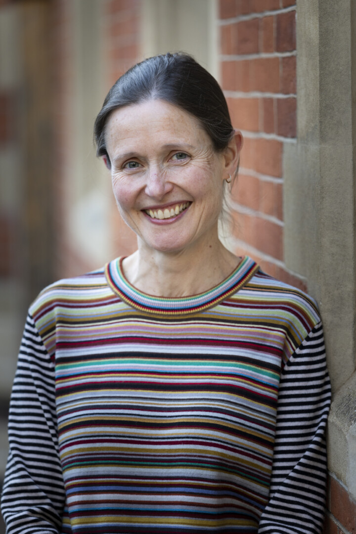 A white woman smiling at the camera. She's wearing a colourful stripey tip and has dark hair tied back into a bun.